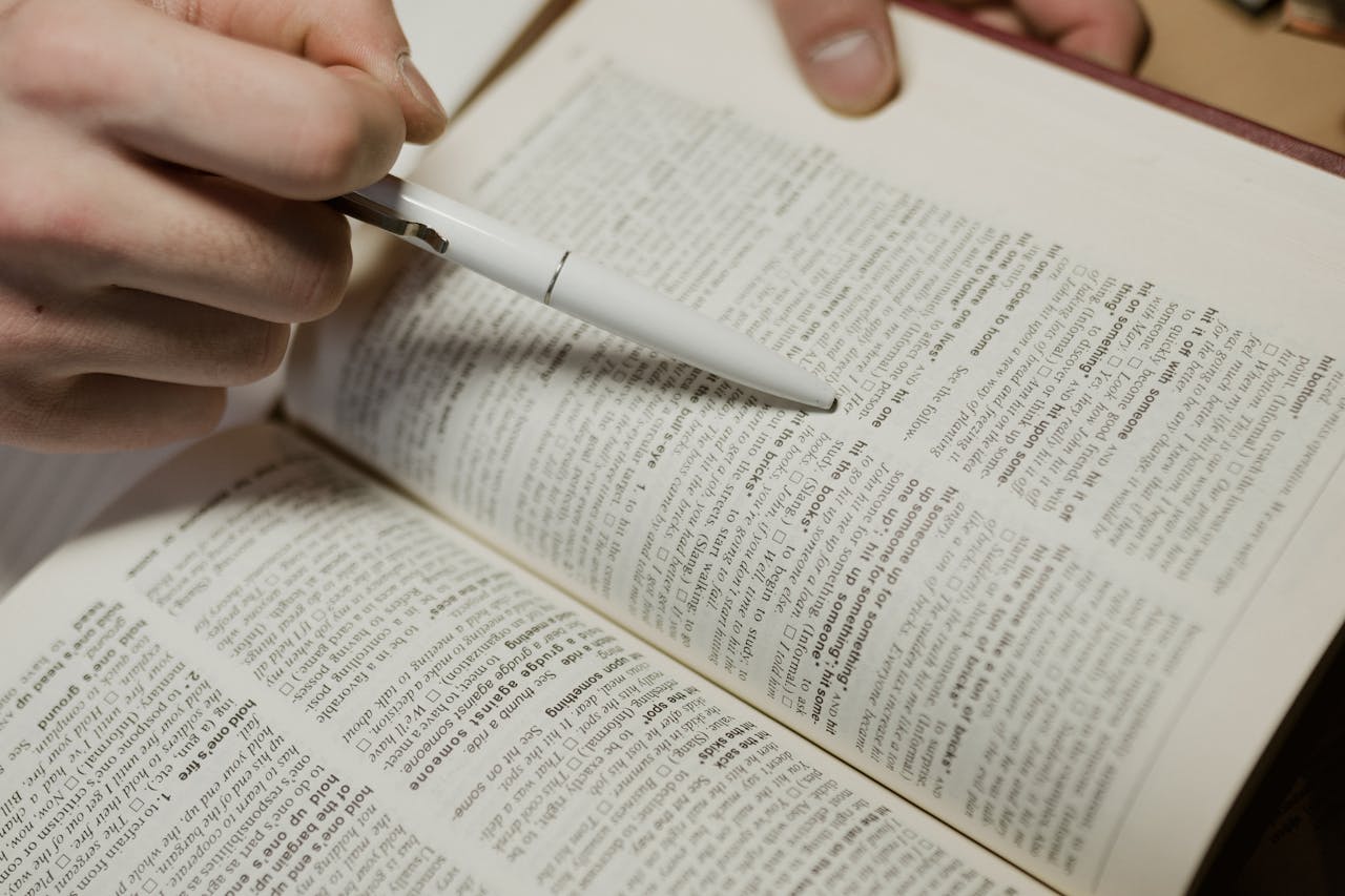 services-03 A close-up image of a hand using a pen to point at text in a book.