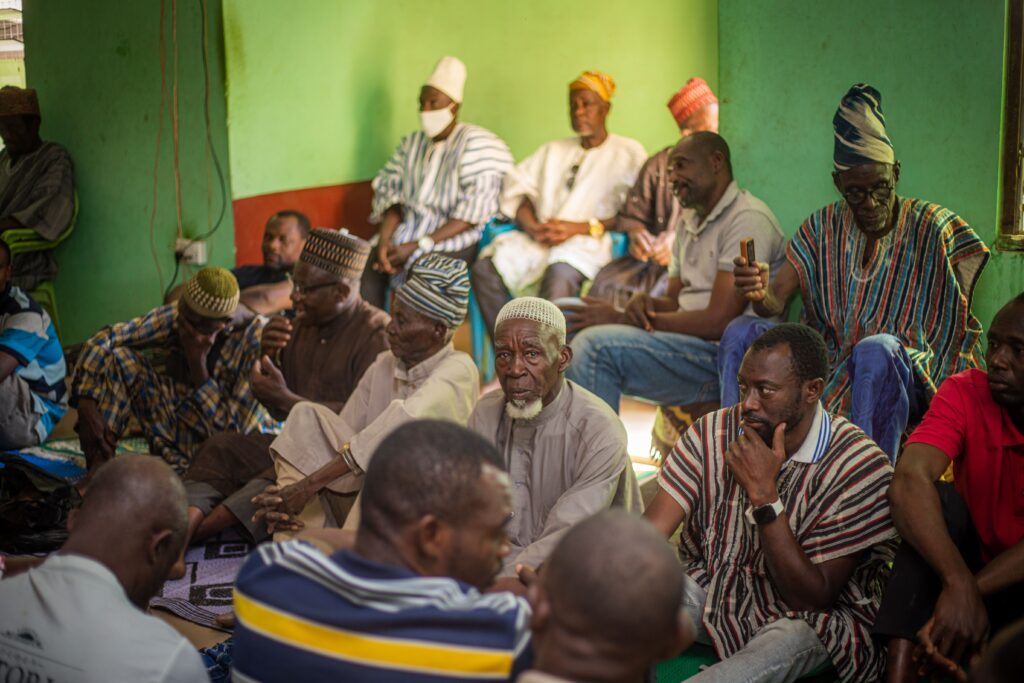 pexels-photo-35845537-35845537 Men sitting together in traditional African clothing in a vibrant green room.
